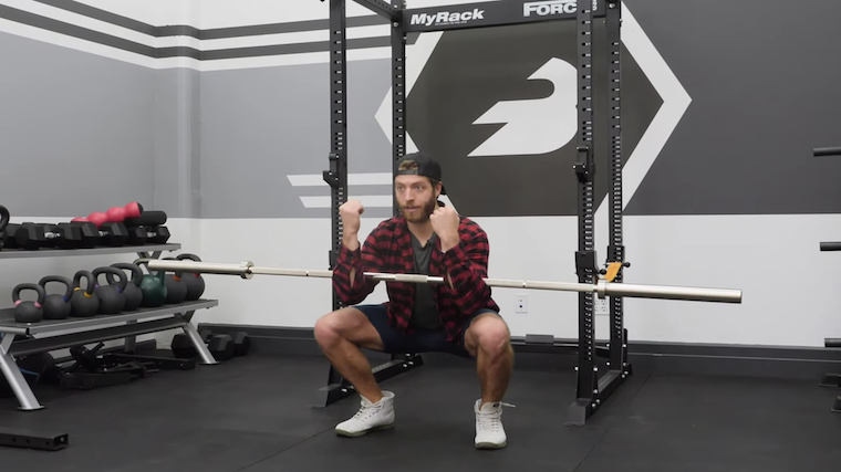 Men performing squat holding barbell in arms