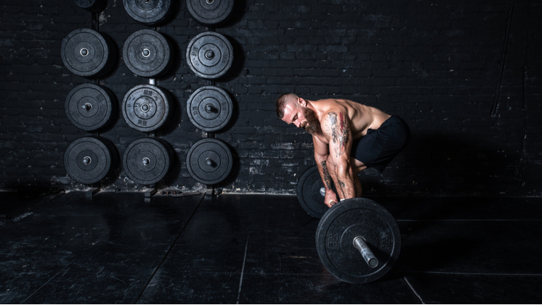 Muscular man picking up barbell in dark gym