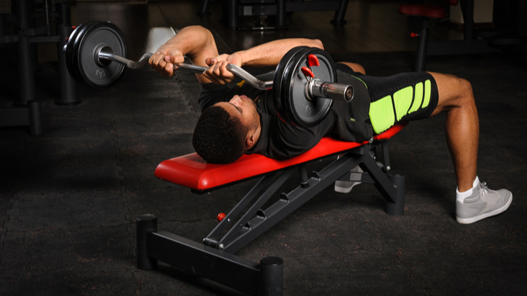 Man in gym performing barbell triceps exercise on flat bench