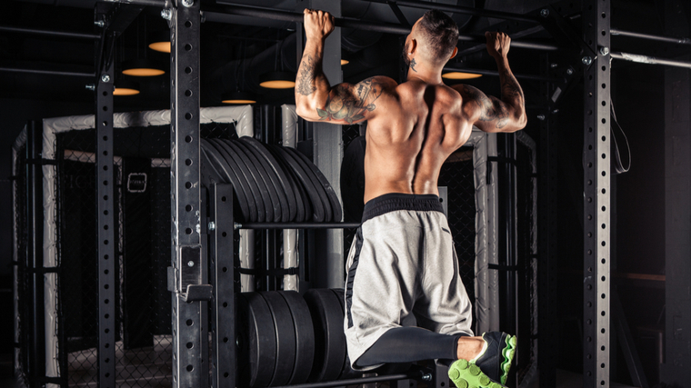 Muscular man performing pull-ups in dark gym