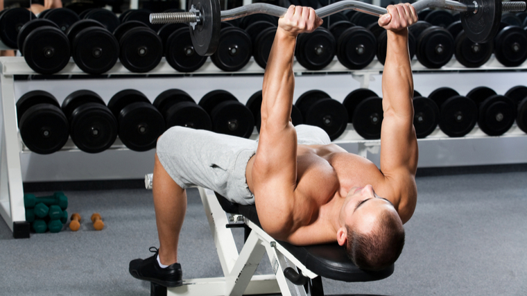 muscular man in gym lying on bench holding barbell above head