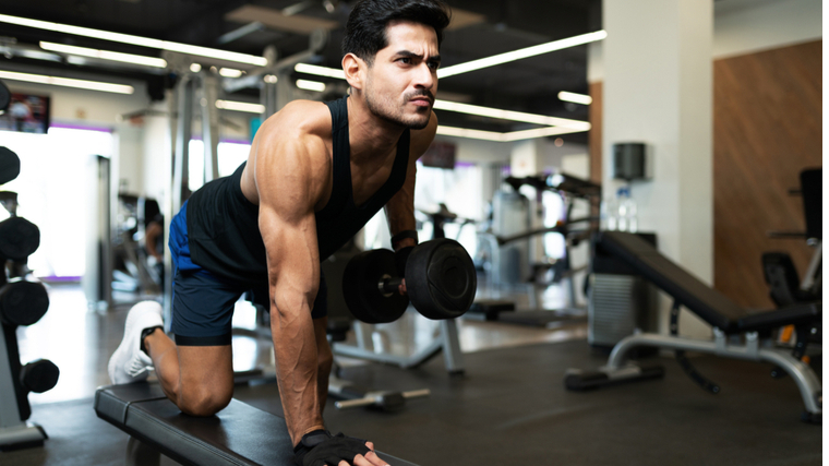 Muscular man in gym rowing dumbbell on bench