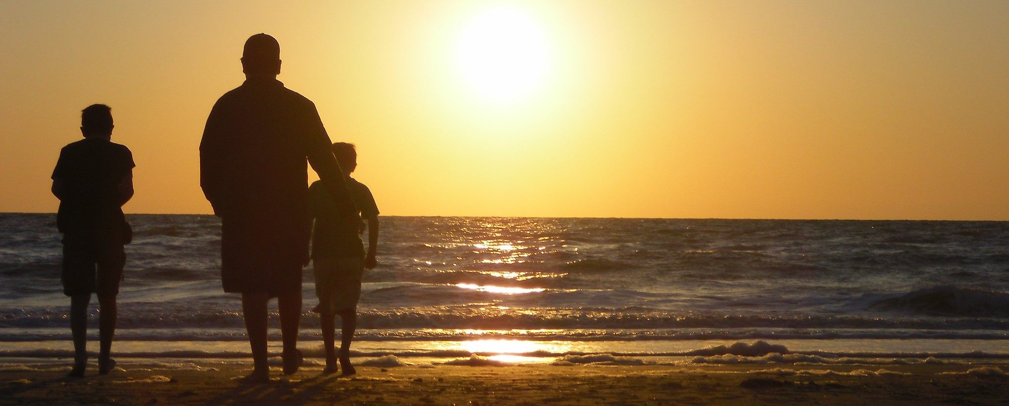 This picture shows a family on the beach looking into the sunset.
