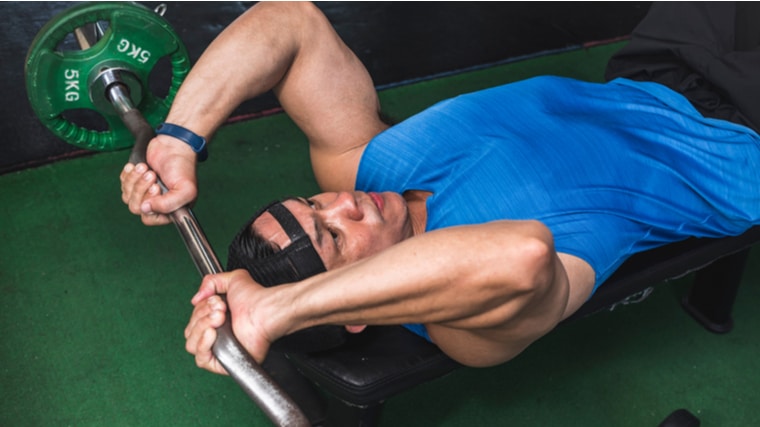 Muscular person lying on bench performing barbell triceps exercise