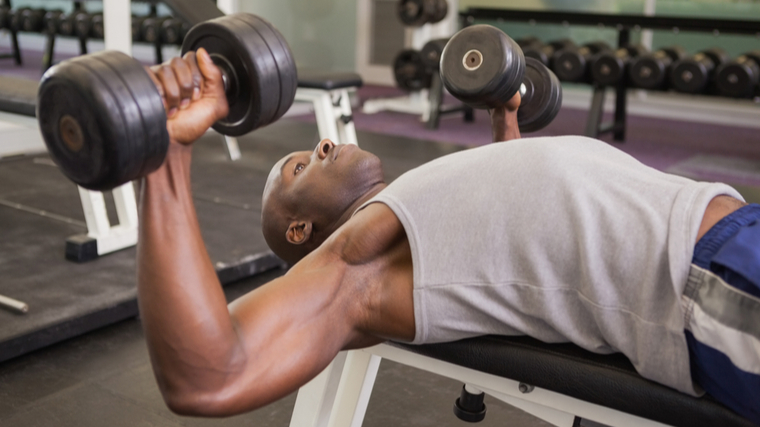 Man in gym performing chest press with dumbbells