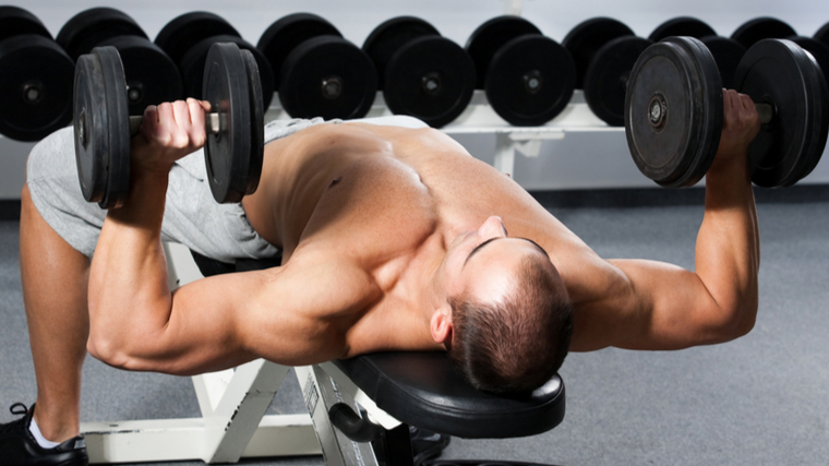 muscular man in gym performing dumbbell chest press