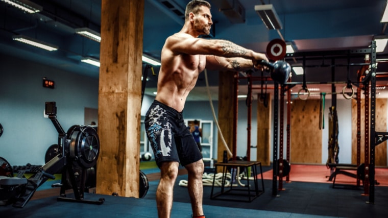 shirtless bodybuilder lifting kettlebell in gym