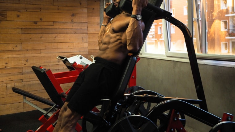 muscular person using squat machine