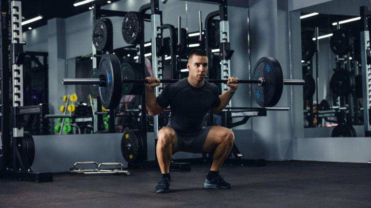 person with barbell squatting in gym