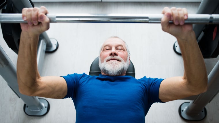 gray-haired person in gym performing bench press