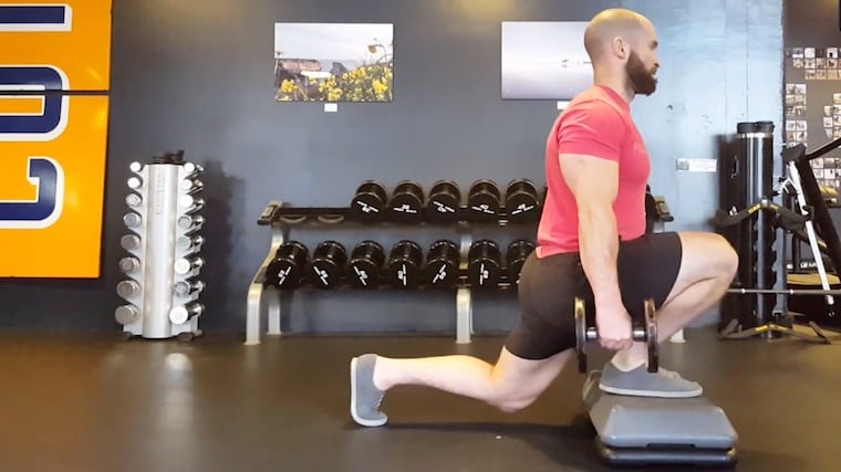 muscular person in gym doing foot-elevated lunge exercise