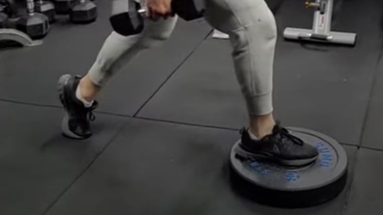 person in gym elevating one foot on weight plate