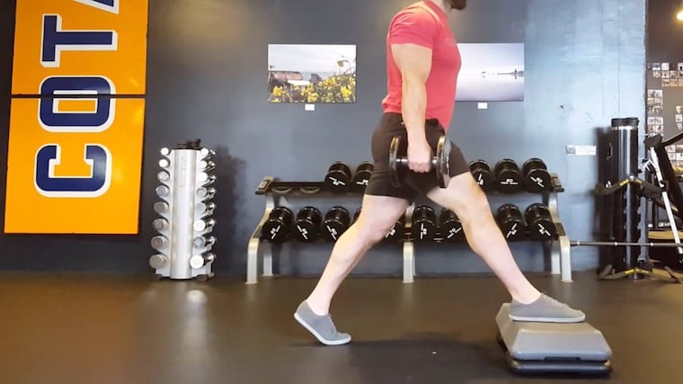 muscular person in gym doing foot-elevated lunge exercise