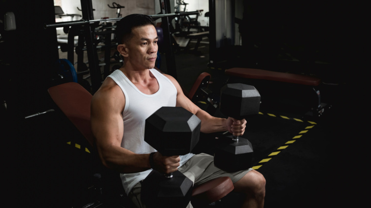 Muscular person in gym sitting on bench holding dumbbells