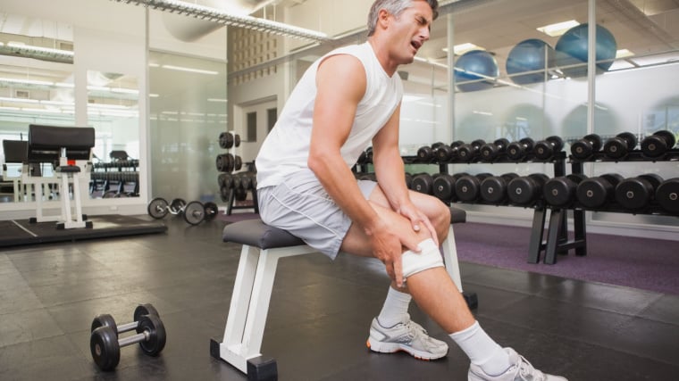 Gray-haired person in gym holding leg in pain