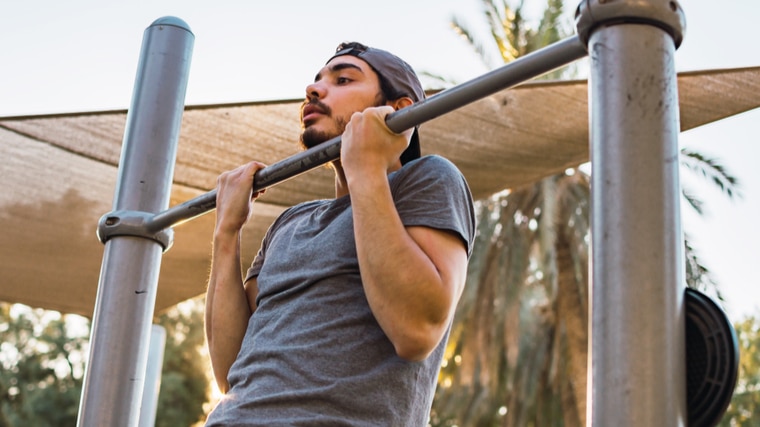 person wearing hat outdoors performing chin-ups