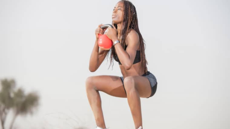 long-haired person outdoors performing kettlebell squat