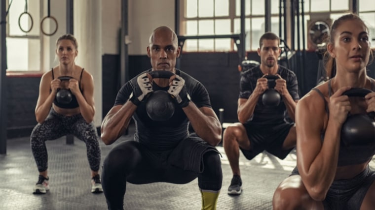 group of people performing squats with kettlebells