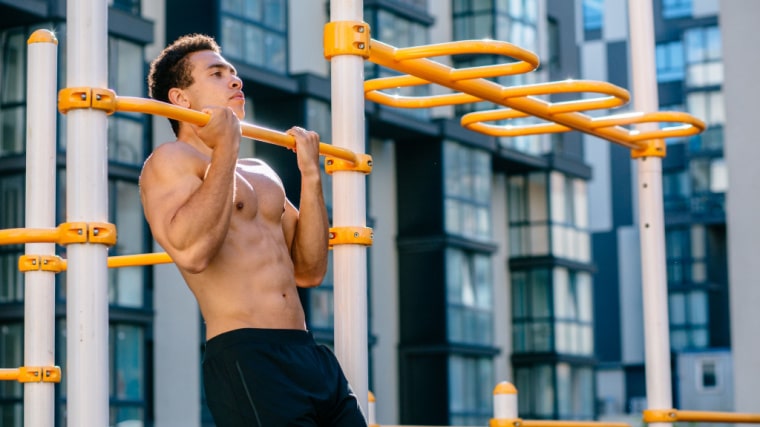 muscular person doing chin-ups outdoors
