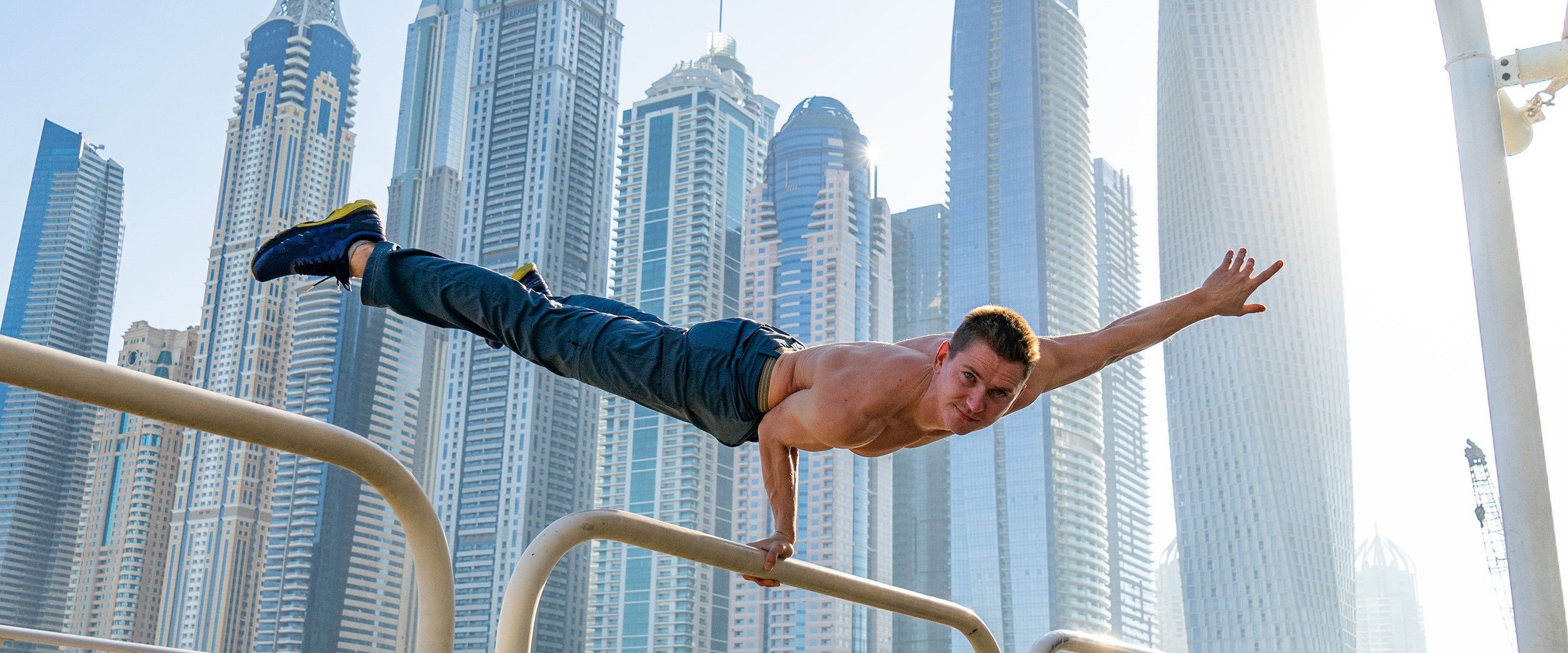 Muscular man doing workout on the street with cityscape of skyscrapers on background in Dubai. Concept of healthy lifestyle and modern