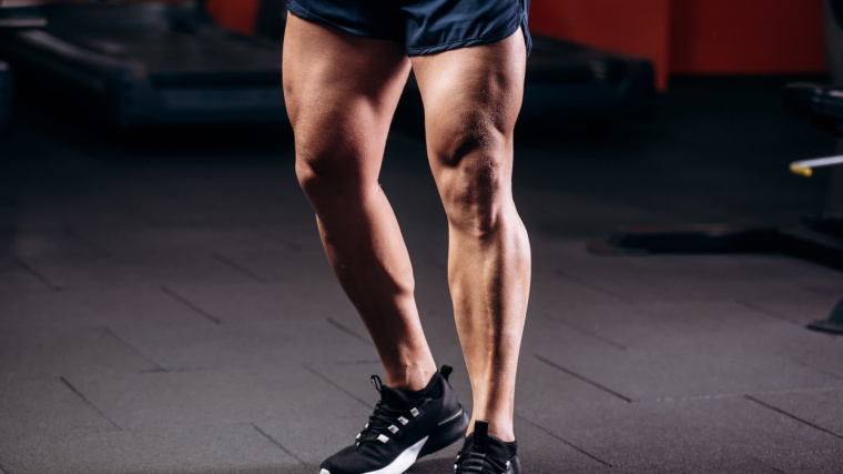 muscular athlete in gym flexing leg muscles